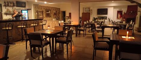 Un restaurante con barra, varias mesas y sillas, y una chimenea al fondo.