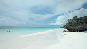 A beach with white sand, clear turquoise water, and a rocky cliff. - Ocean Views, Private Pool, and Lush Botanical Garden  (Governor's Harbour)