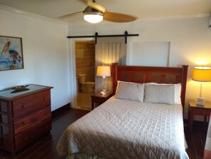 A hotel room with a bed, a wooden dresser, a nightstand with a lamp, a ceiling fan, and a painting on the wall. - Ocean Views, Private Pool, and Lush Botanical Garden  (Governor's Harbour)