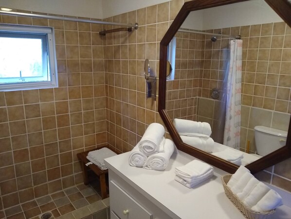 A bathroom with a tiled shower wall, a window, a mirror, and towels on the counter.