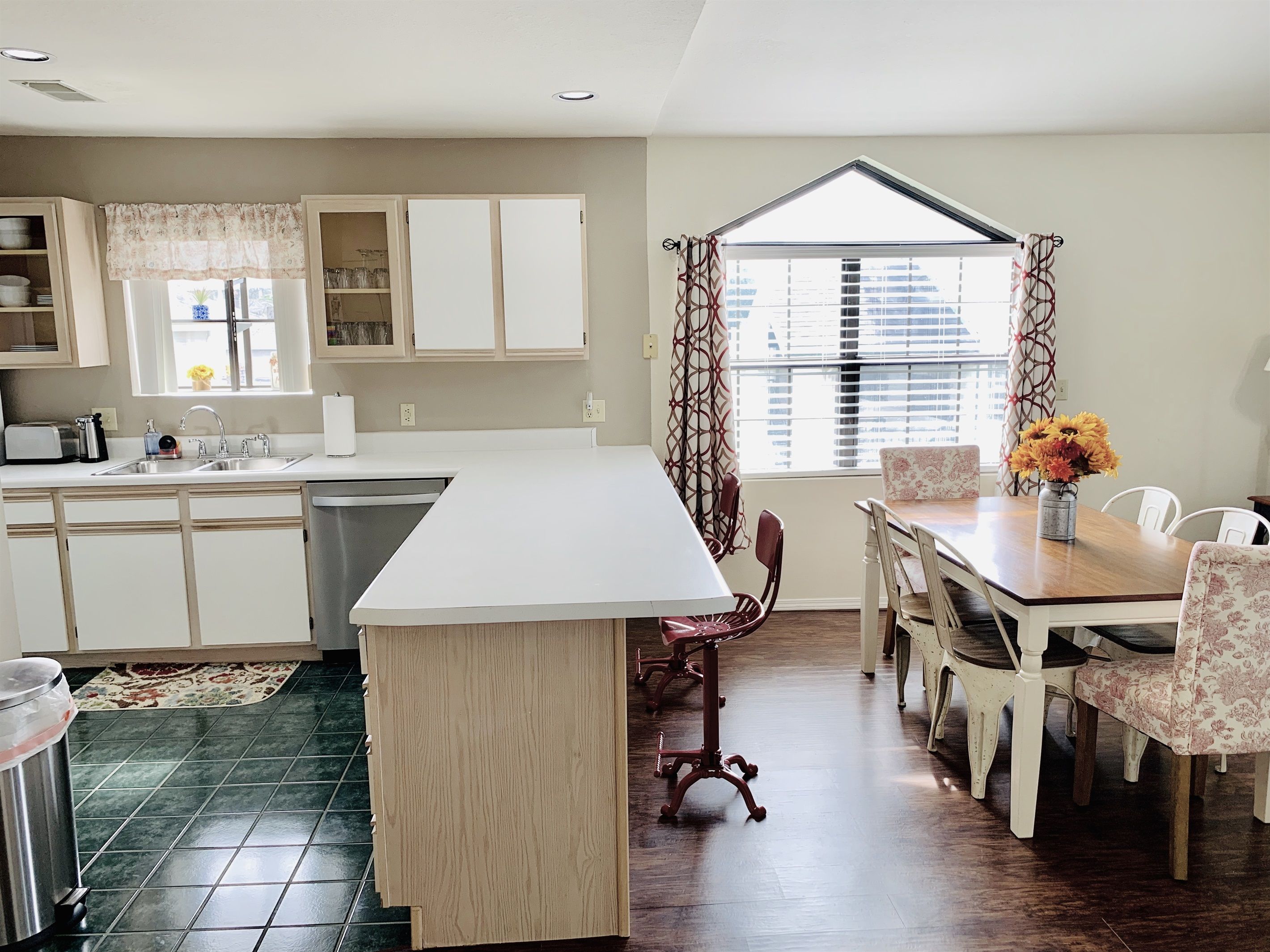 A kitchen with a central island, a dining area with a table and chairs, and a window with curtains.