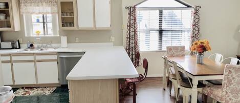 A kitchen with a central island, a dining area with a table and chairs, and a window with curtains.