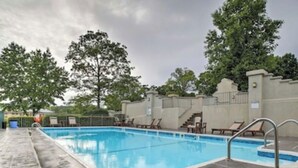 Una piscina rectangular con solárium alicatado, rodeada de sillas de descanso y una zona cubierta con escaleras.