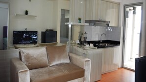 Una sala moderna con sofá, televisor, zona de cocina con lavaplatos y estufa, y puerta de vidrio que da a un balcón.