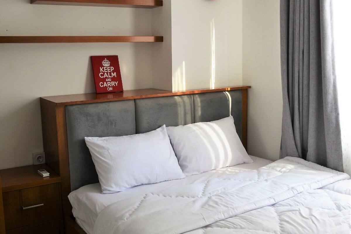 A neatly made bed with white bedding, a wooden headboard, and a red sign on the wall.
