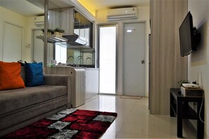 A compact living space with a sofa, a small kitchen area, and a television mounted on the wall.