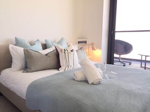 A neatly made bed with a blue and white striped blanket, multiple pillows in various patterns, and a rolled white towel on the bed. - Deluxe and Brand New Lakeside Apartment (Melbourne)