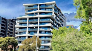 A modern multi-story building with balconies, surrounded by trees and other buildings. - Deluxe and Brand New Lakeside Apartment (Melbourne)