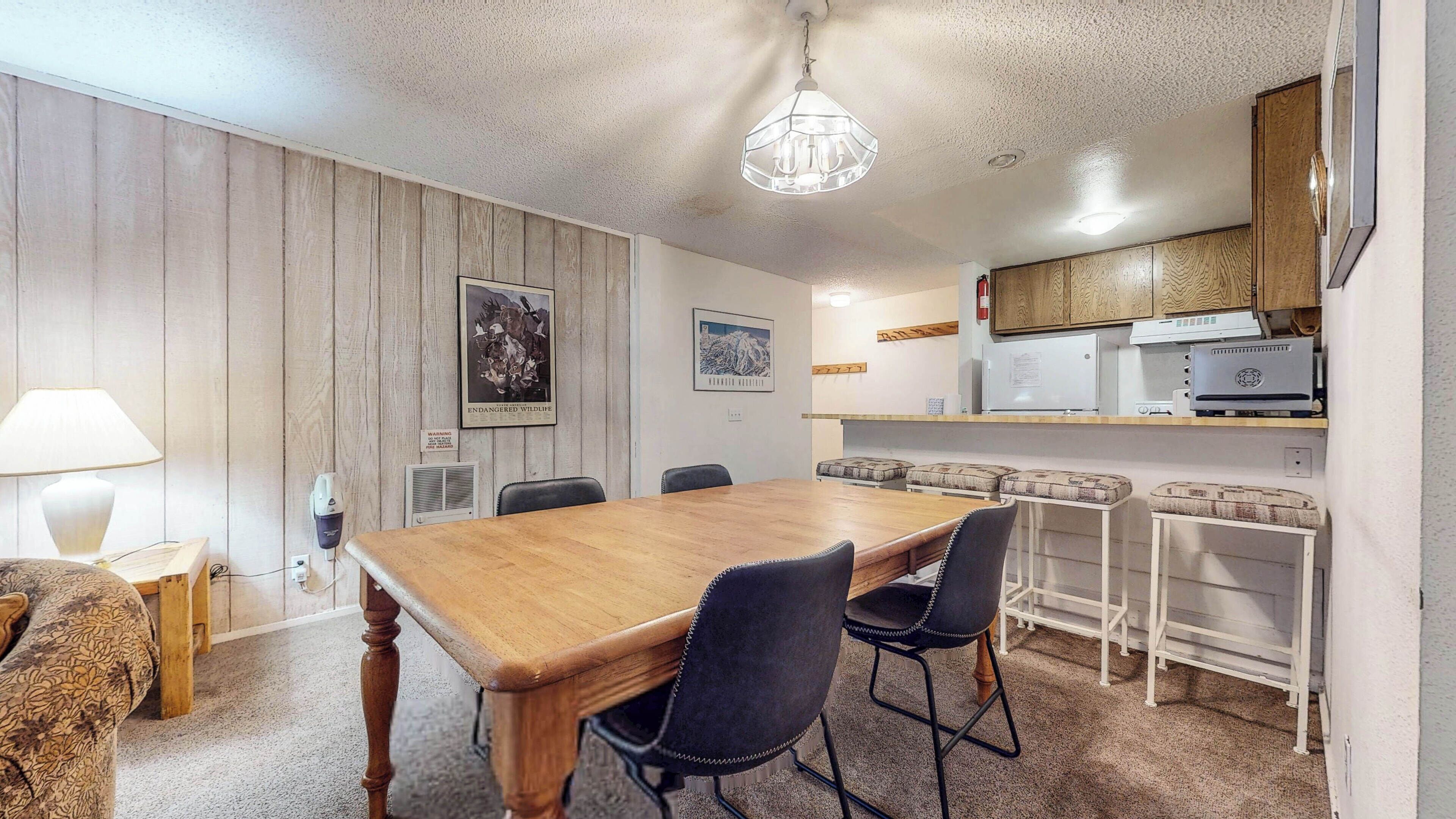 A dining area with a wooden table and chairs, a kitchen with wooden cabinets, and a ceiling light fixture.