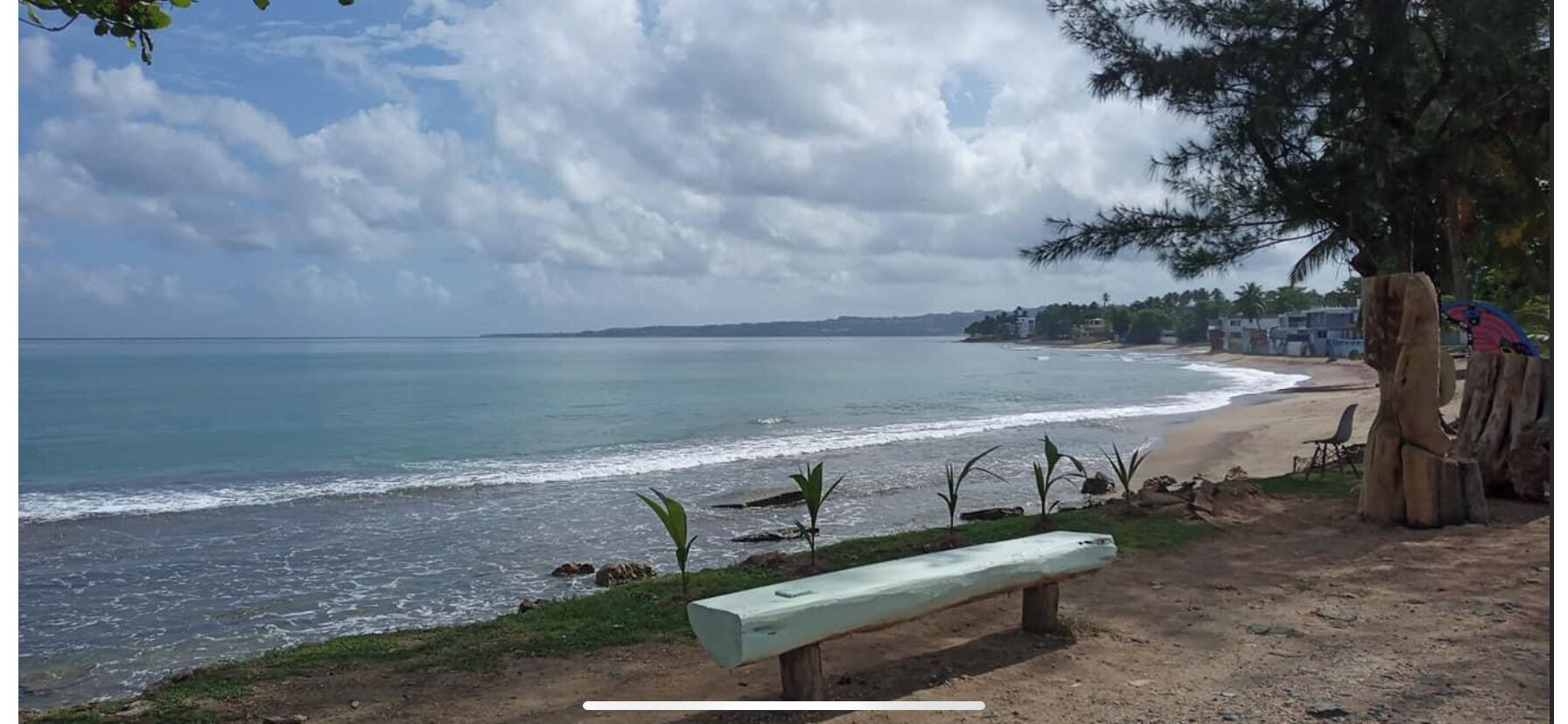 Una playa con un banco, una estructura de madera y vistas al océano.