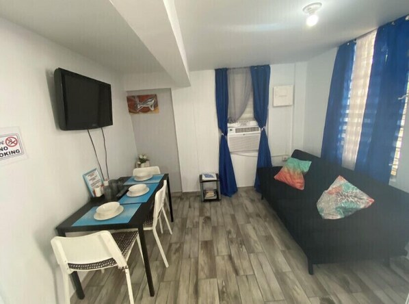 A compact living space with a dining area, a sofa, a flat-screen TV, and a no-smoking sign.