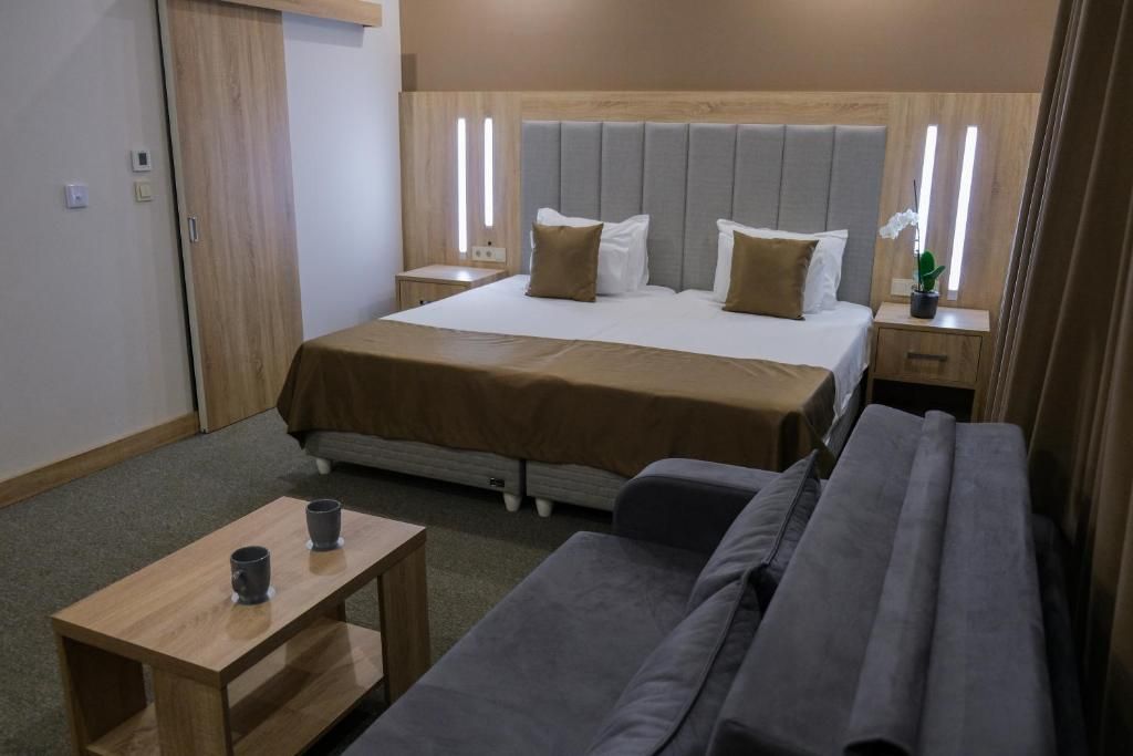 A hotel room with a bed, bedside tables, a sofa, and a small table with two cups.