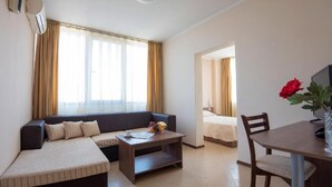Ein Hotelzimmer mit Sofa, einem kleinen Tisch mit Blumenvase, einem Bett und einem Esstisch.