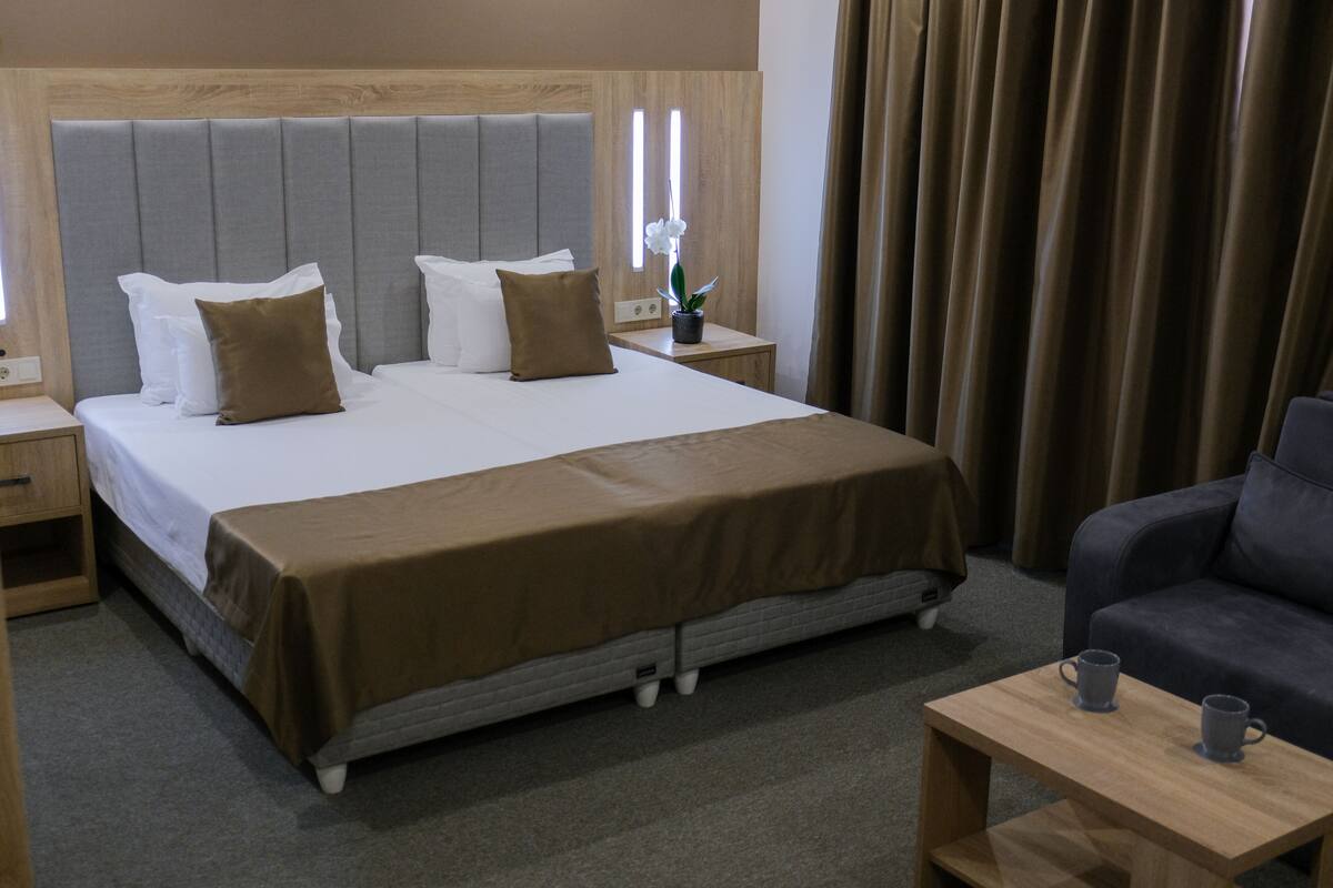 Ein Hotelzimmer mit einem großen Bett, einem Nachttisch mit Lampe, einem kleinen Tisch mit zwei Tassen und einem Sofa.