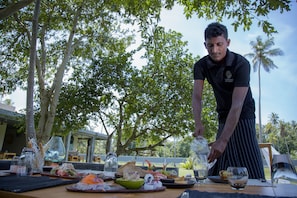 A person serving food at an outdoor dining table with various dishes and drinks. - Wirdana Resort & Spa (Boossa)