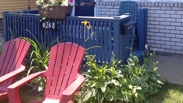 Een huis met een bakstenen gevel, een blauwe deur en een brievenbus met het nummer 4268. Twee rode Adirondack-stoelen staan ervoor.