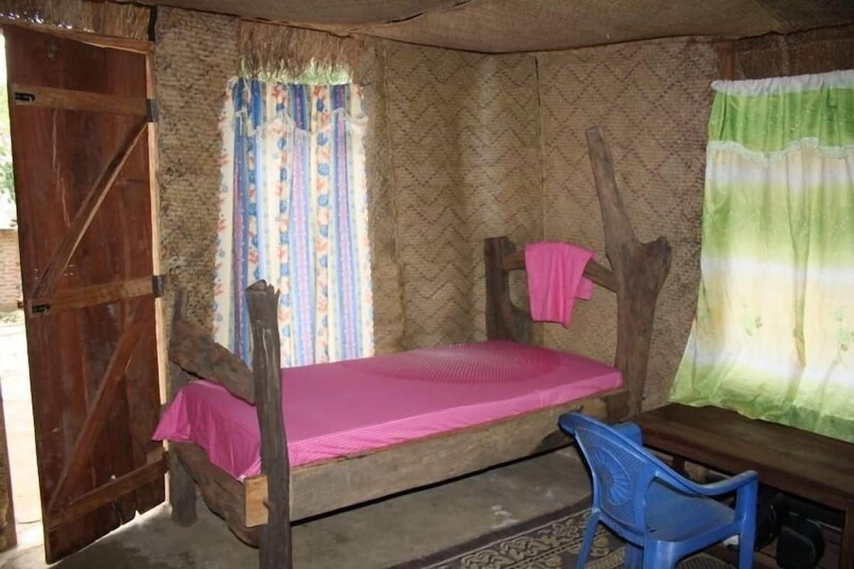A rustic room with a wooden bunk bed, a small table, a chair, and a window with patterned curtains.