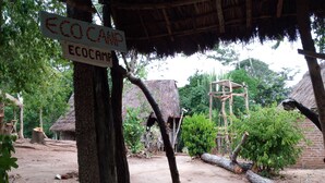An eco camp with thatched-roof huts, a wooden structure, and a sign indicating the camp's name. - Ngerengere River Eco camp (Ubena Bwawani)