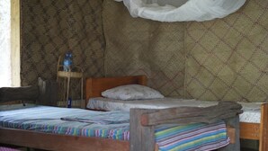 A rustic room with two wooden beds, a woven chair, and a water bottle on a small table. - Ngerengere River Eco camp (Ubena Bwawani)