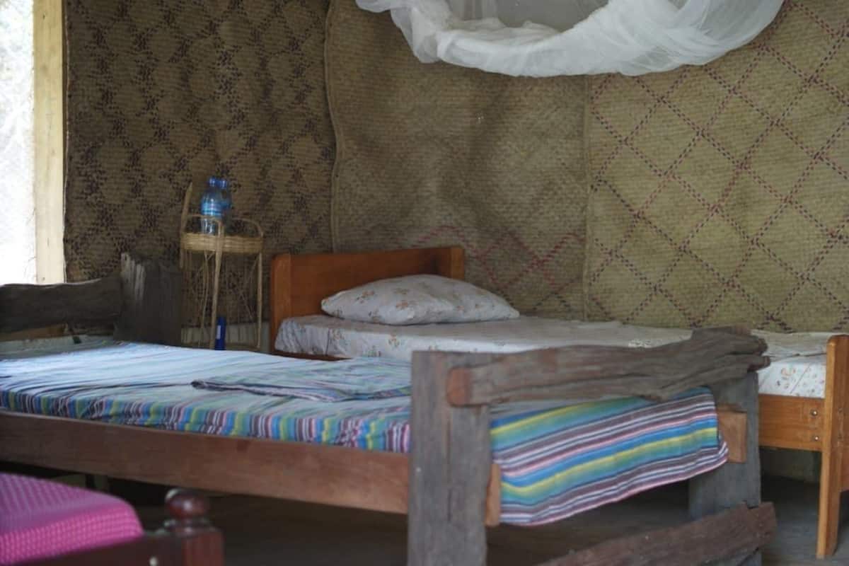 A rustic room with two wooden beds, a woven chair, and a water bottle on a small table.