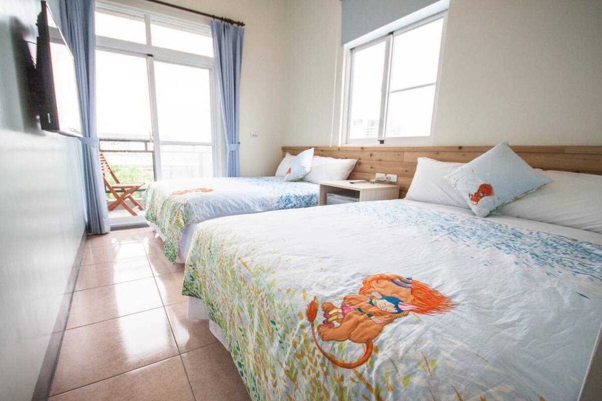 A hotel room with two beds, a wooden headboard, a small table, and a window with curtains.