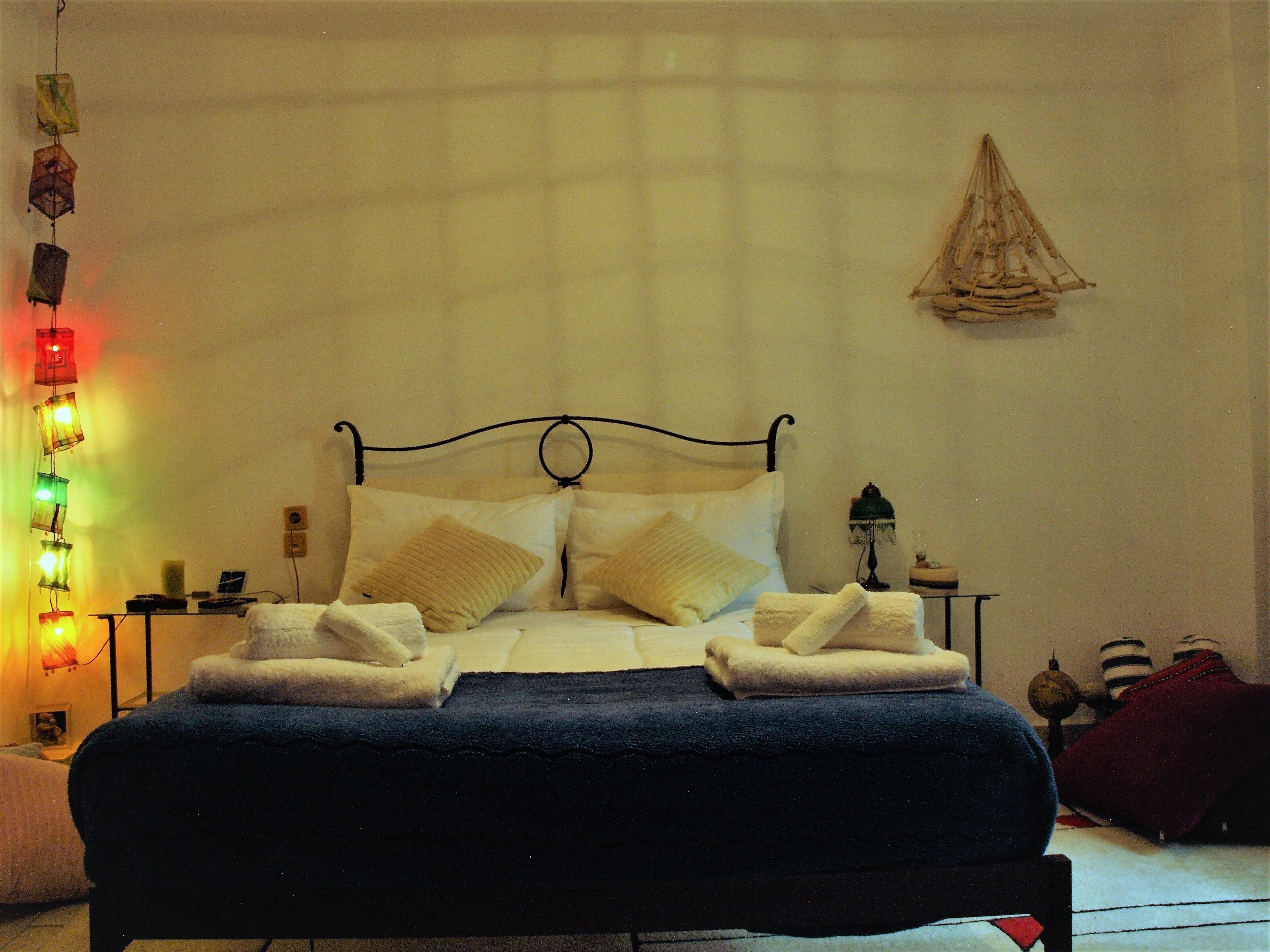 A neatly made bed with a dark blue blanket and two white towels, a bedside table with a lamp, and a wall-mounted decorative item.