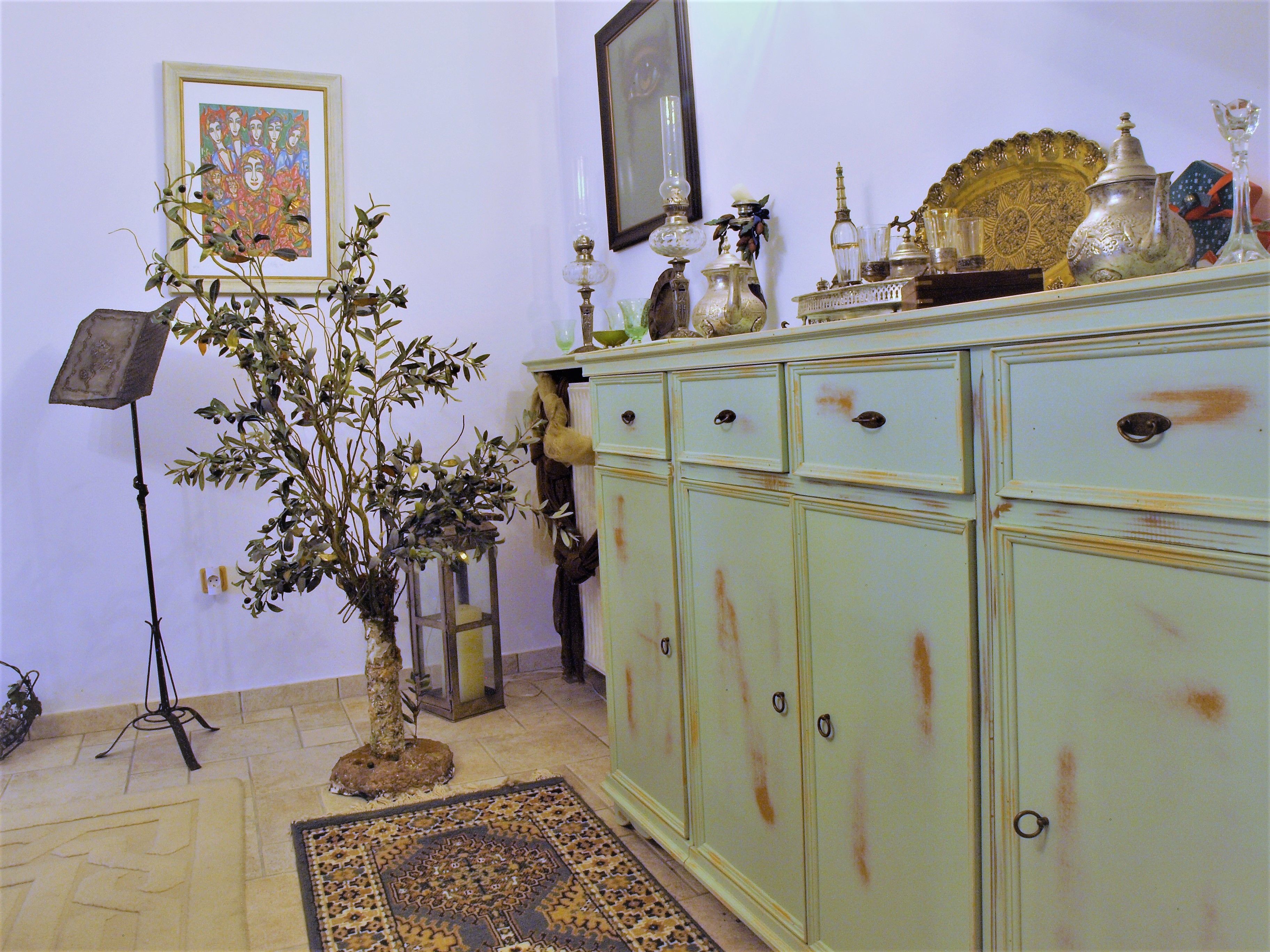 A room with a cabinet, a framed artwork, a plant, and a lamp.