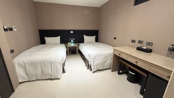 A hotel room with two beds, a desk, a nightstand, and a small table with a lamp.