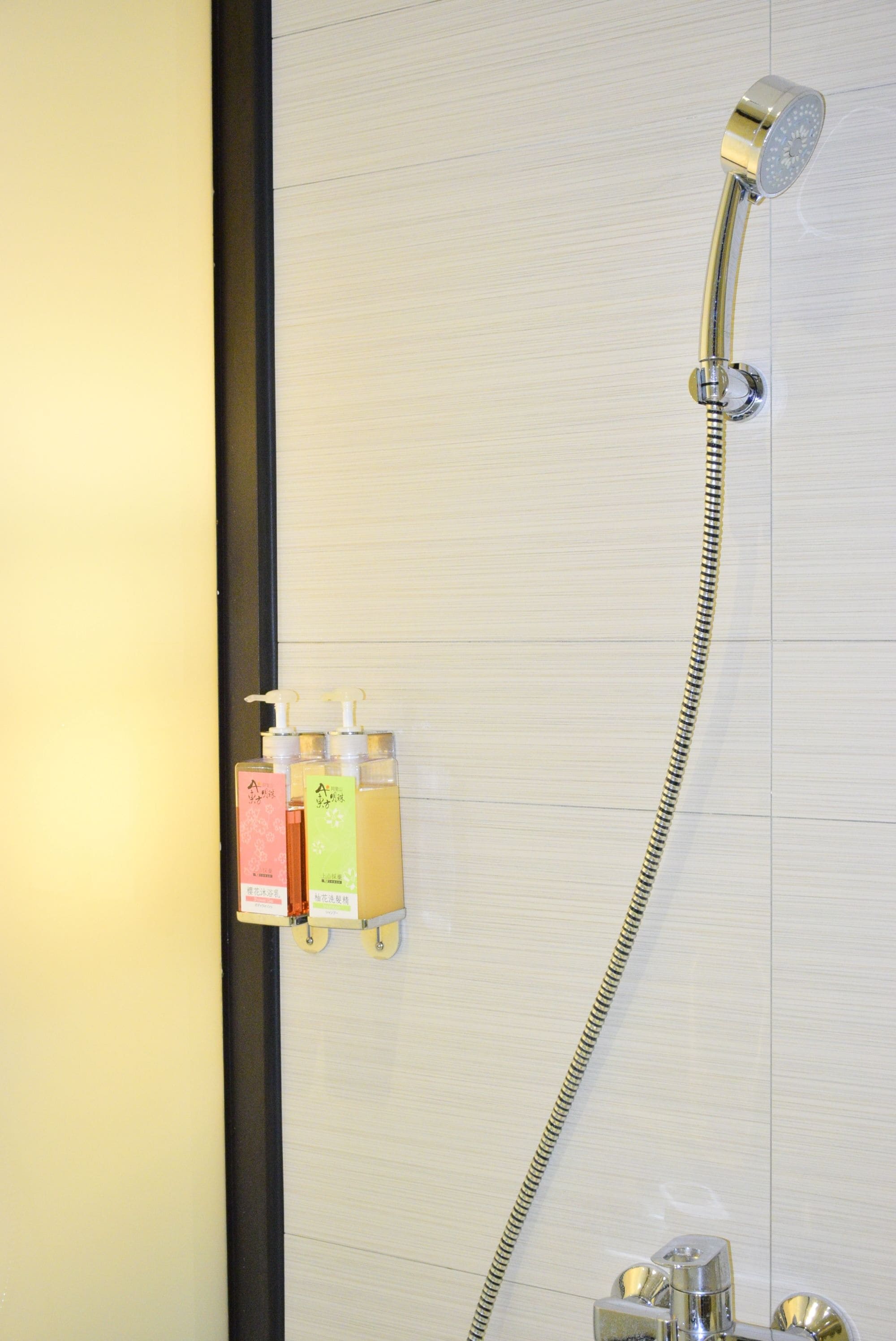 Een douche met een handdouche en een flexibele slang. Drie flessen shampoo en conditioner staan op de muur.