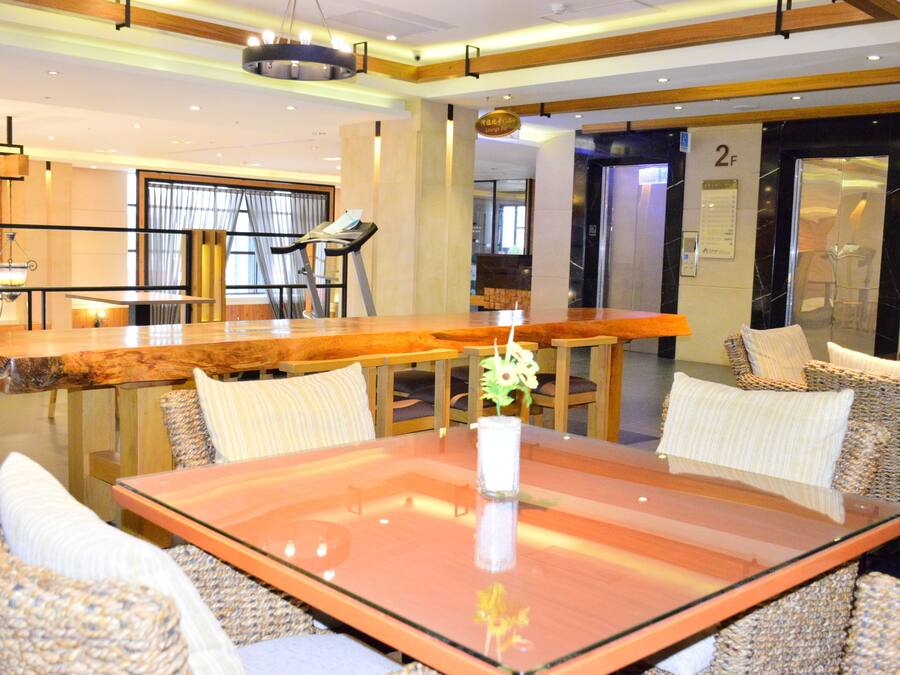 Um hall de hotel moderno com uma mesa de vidro, cadeiras de vime, esteira e um balcão de recepção.