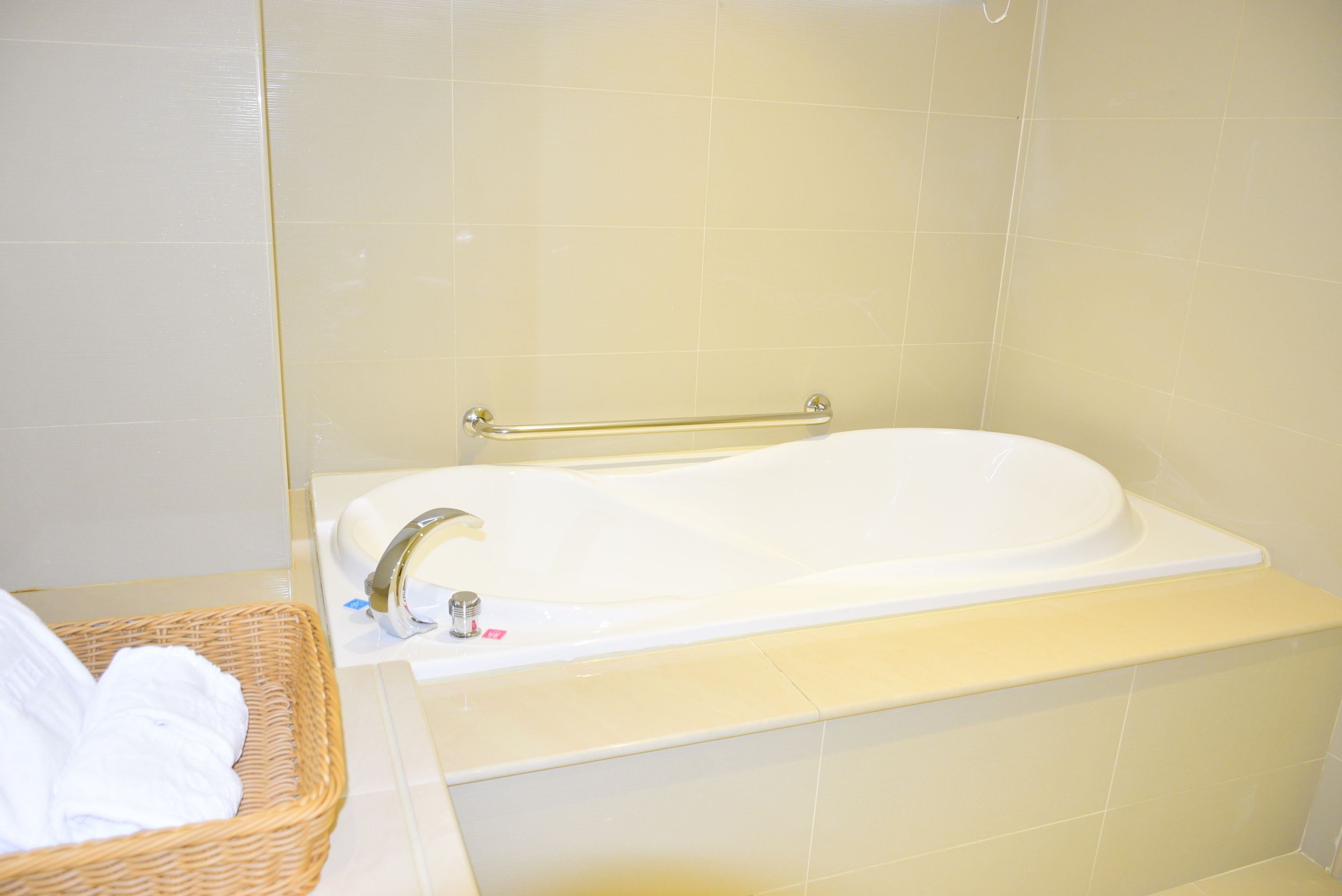 Un baño con una bañera blanca, un pasamanos dorado y una cesta de mimbre con toallas blancas.