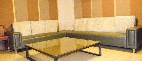 Una sala de estar con un sofá seccional, una mesa de centro de vidrio y una mesita auxiliar.