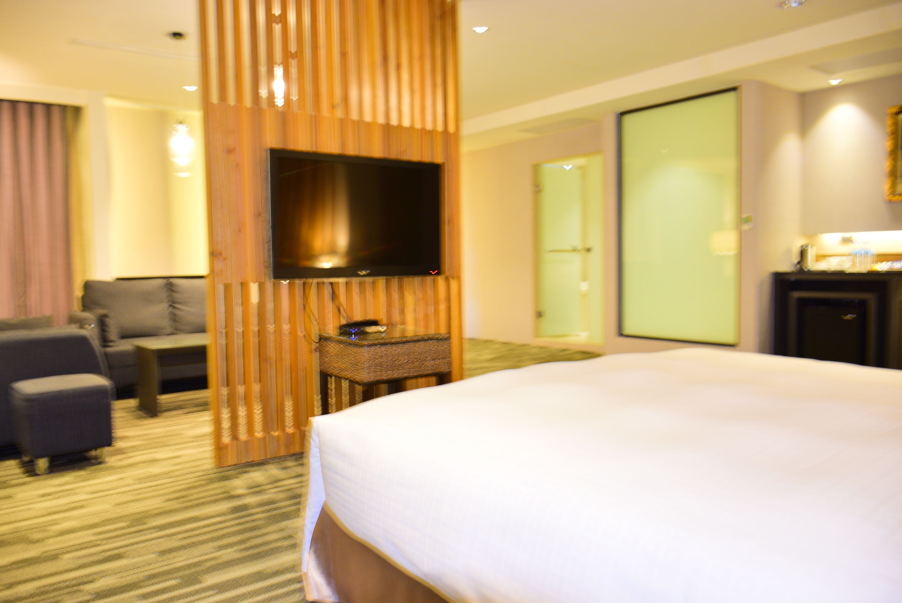 Ein Hotelzimmer mit einem großen Bett, einem an einer Holzplatte montierten Flachbildfernseher, einer Couch, einem kleinen Tisch und einer Tür zu einem Badezimmer.