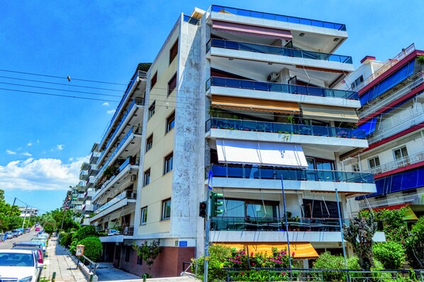Un immeuble à plusieurs étages doté de balcons, donnant sur une rue passante et bordé de voitures garées.