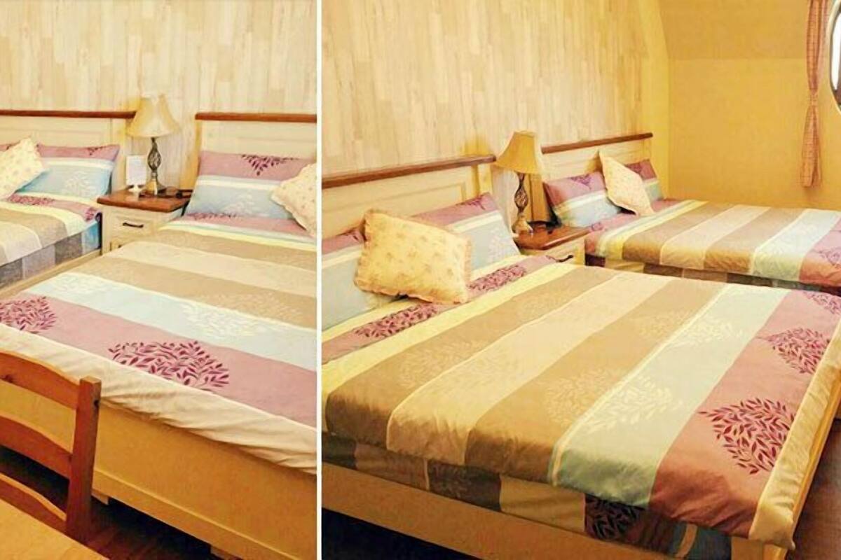 Quarto de hotel com duas camas, cada uma com cabeceira de madeira, mesa de cabeceira e abajur. Há uma janela com cortinas.