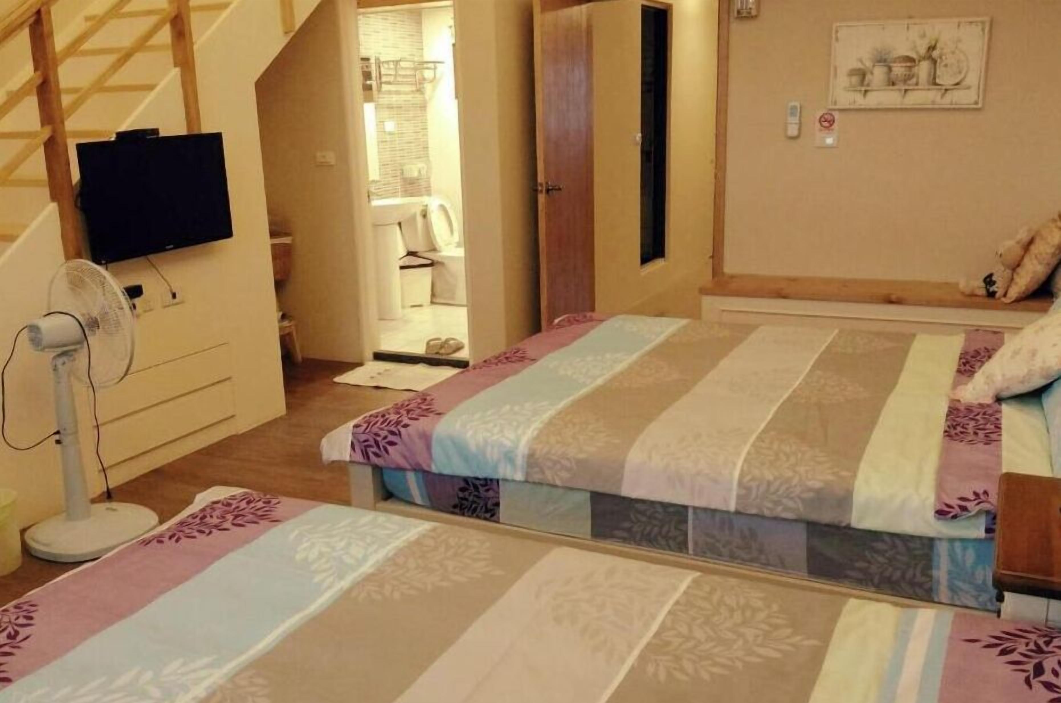 Une chambre à coucher avec un lit, une télévision, un ventilateur, et une salle de bain visible au fond.