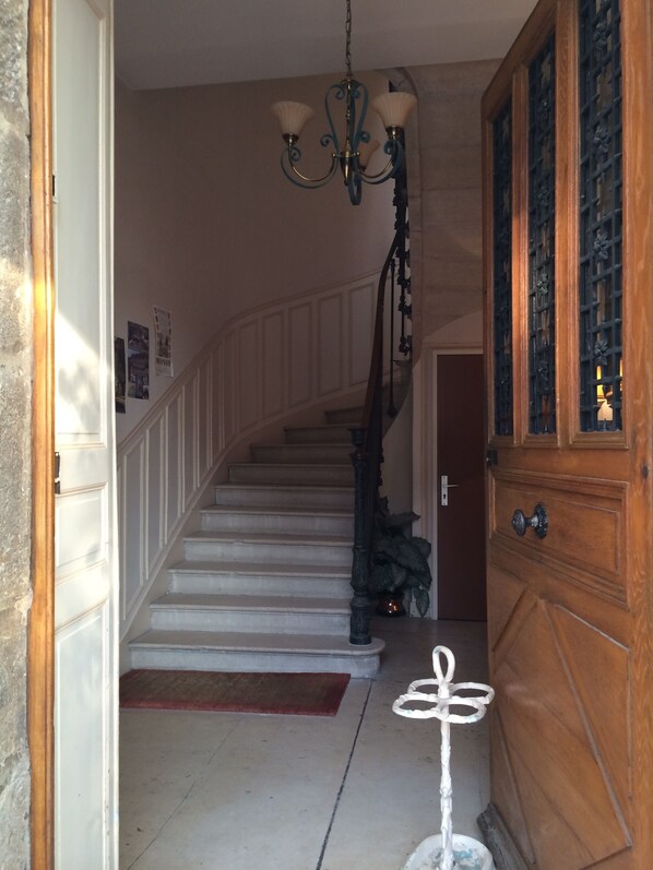 A staircase with white steps and a wooden railing, leading to a room with a wooden door and a decorative panel. - Hôtel des Cymaises (Semur-en-Auxois)