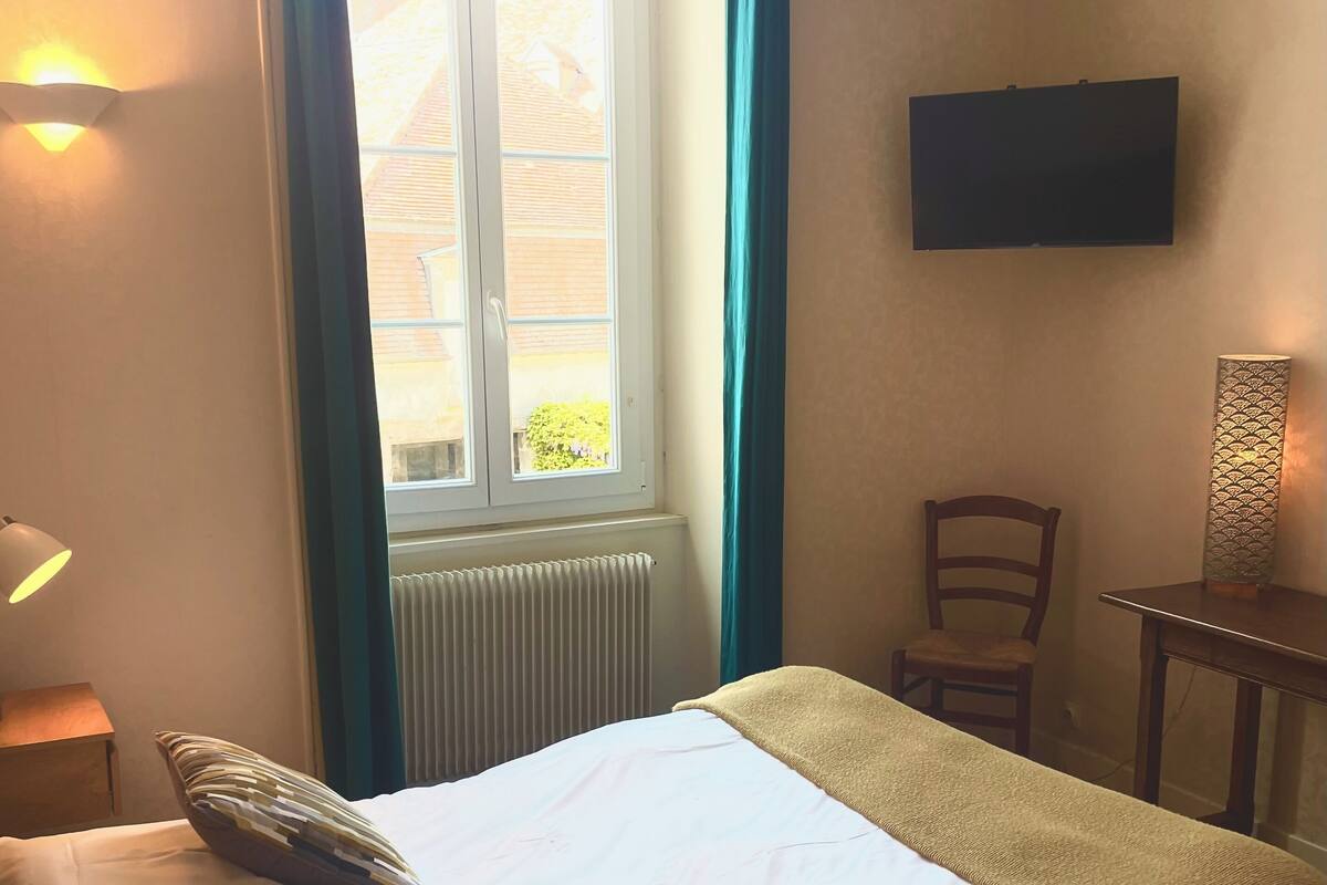 Una habitación de hotel con cama, una silla, una mesa, televisión y ventana con cortinas.