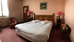 Een hotelkamer met een groot bed, een stoel, een klein tafeltje met een lamp en een radiator.