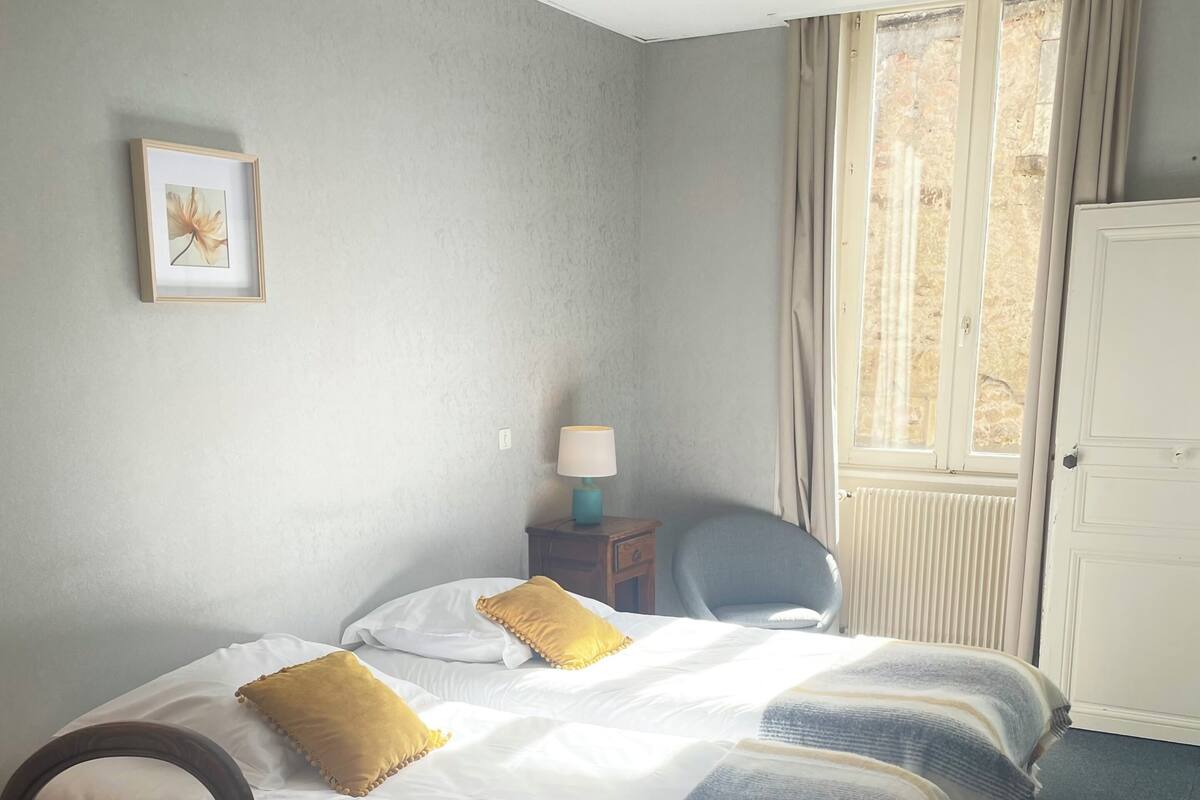 Habitación de hotel con cama, una silla, una mesa, una lámpara, un cuadro en la pared y una ventana con cortinas.