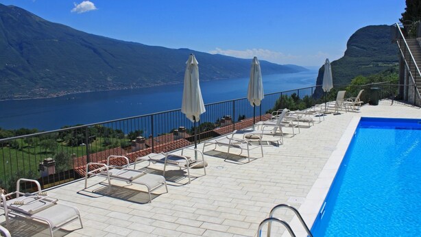 A poolside area with lounge chairs and umbrellas, overlooking a lake and mountains.