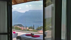 A balcony with a table and chairs, overlooking a mountainous landscape and a body of water.