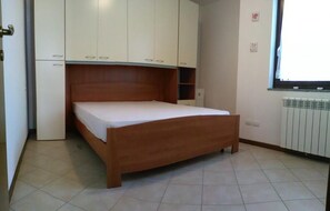 A bedroom with a wooden bed, white cabinets, and a radiator. - La Quiete 16 Holideal (Tremosine)