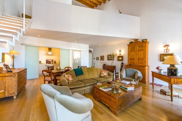 A spacious living room with a high ceiling, wooden staircase, and a dining area with a table and chairs.