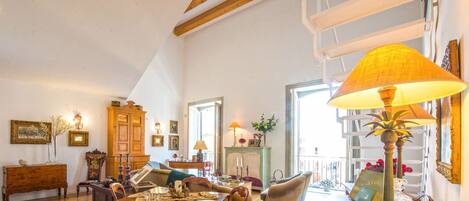 A spacious living room with a dining area, wooden furniture, and a large window providing natural light.