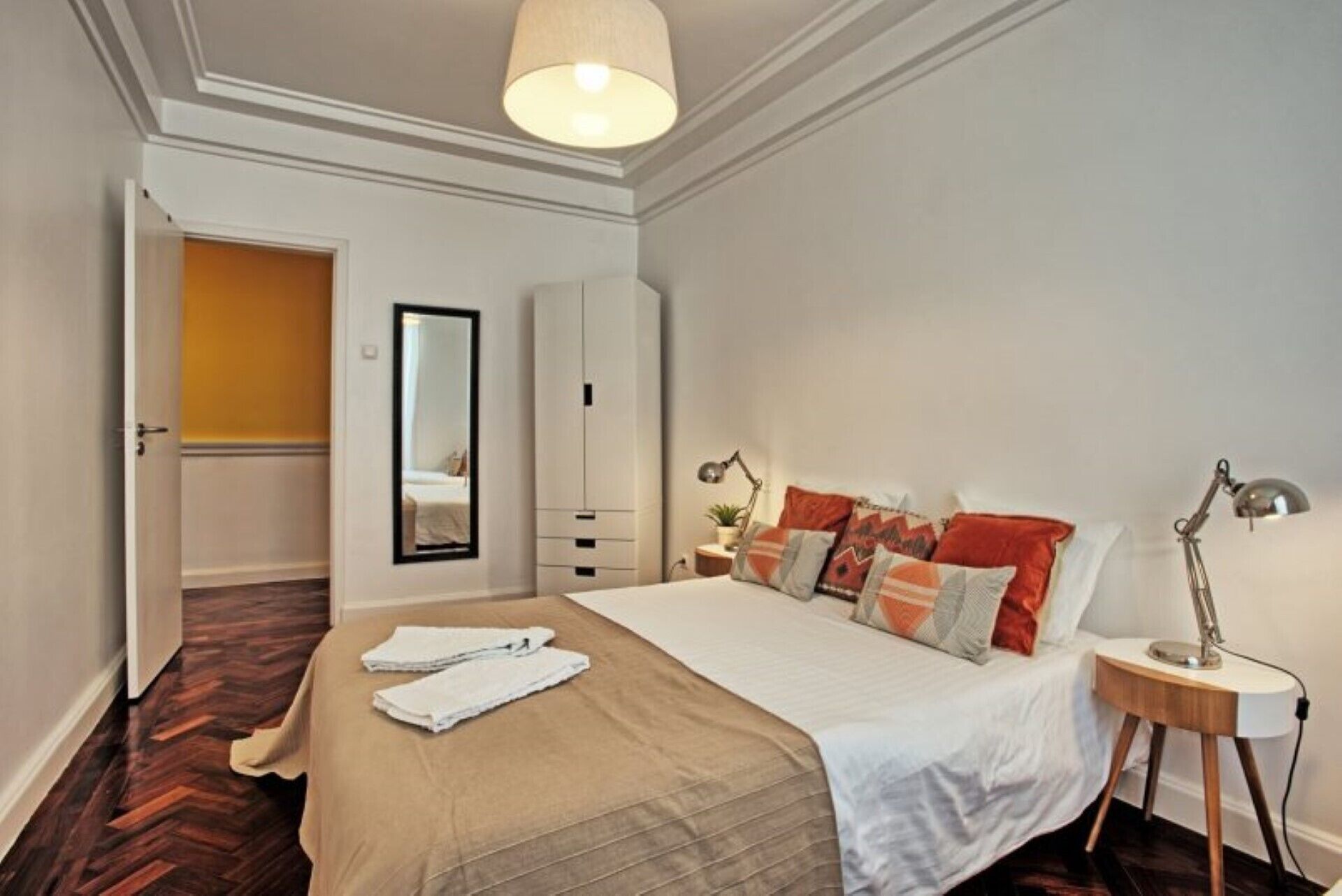 A bedroom with a bed, bedside lamps, a wardrobe, and a mirror.