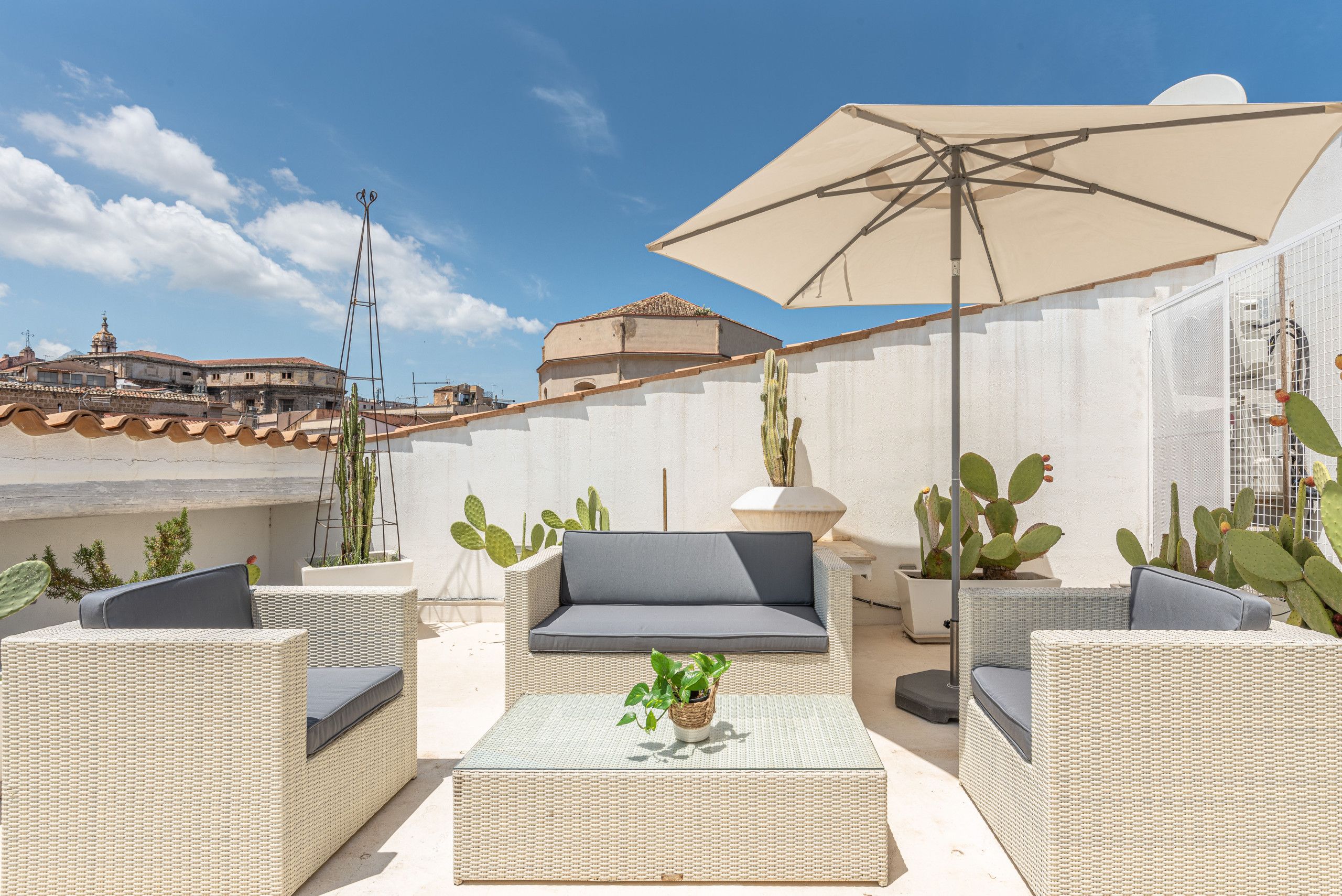 Un patio en la azotea con mobiliario de mimbre, un parasol grande y cactus.