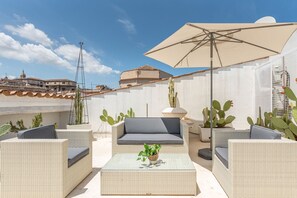 A rooftop patio with wicker furniture, a large umbrella, and cacti. - Cala Loft by Wonderful Italy (Palermo)