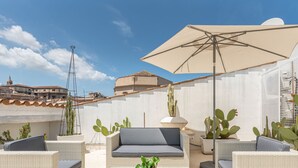 Une terrasse sur le toit, aménagée avec des meubles en osier, un grand parasol et des cactus.