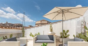A rooftop patio with wicker furniture, a large umbrella, and cacti.